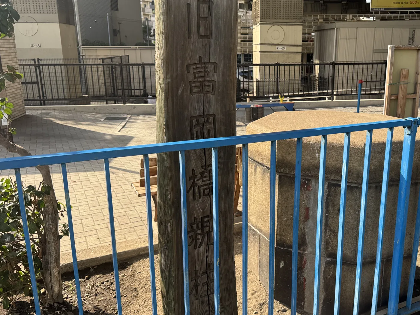 「旧富岡橋親柱」と刻まれた木製案内柱と石の親柱
