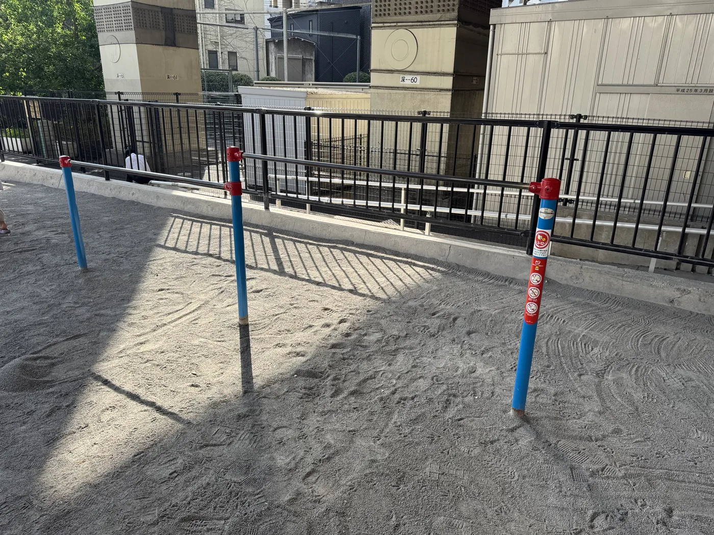 青い支柱の鉄棒が並ぶ油堀川公園の砂場