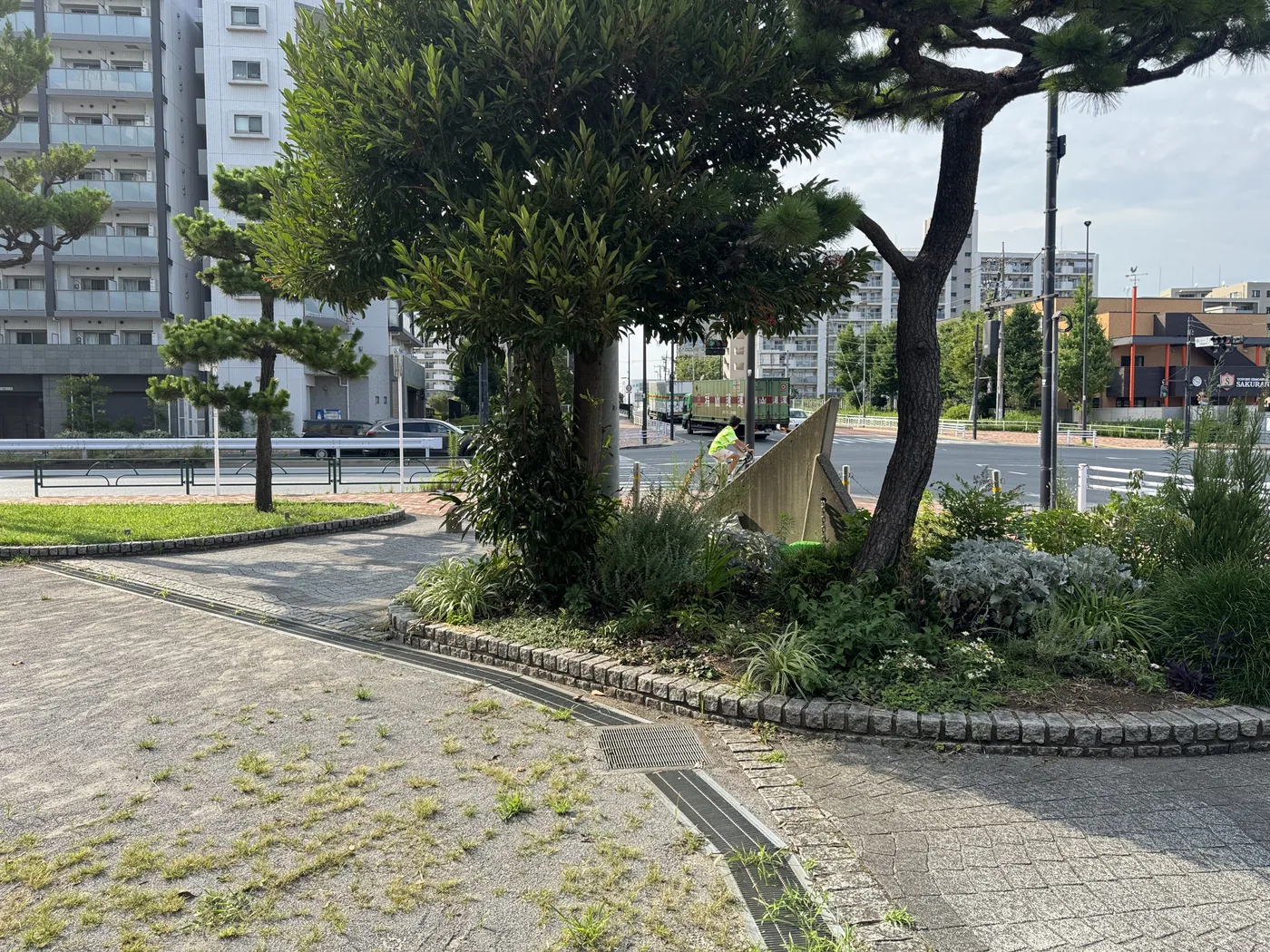 交差点側の植栽帯と帆形モニュメント。舗装された広場