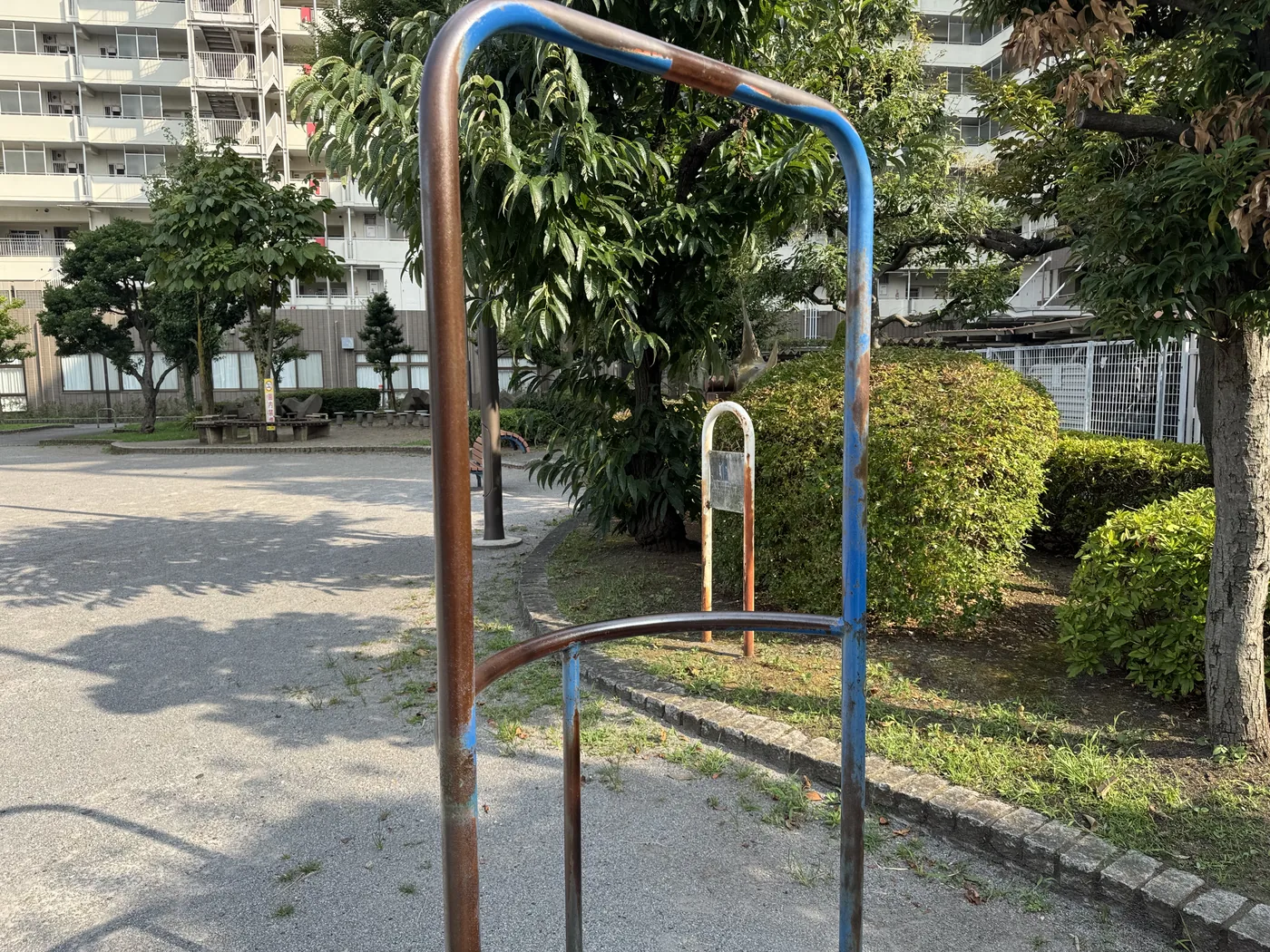 青い塗装が剥げた健康遊具のフレーム。背後に集合住宅