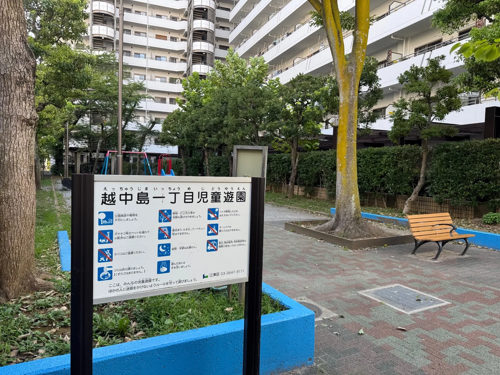 越中島一丁目児童遊園の利用案内板と木のベンチ、青い縁石
