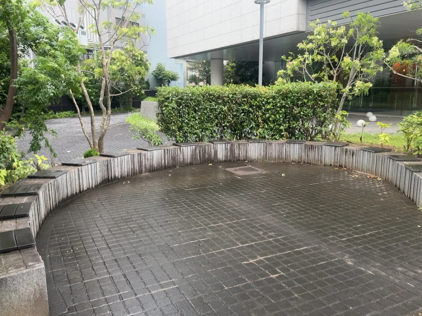 半円に並んだコンクリートのベンチと石畳、黄色い園内禁煙看板