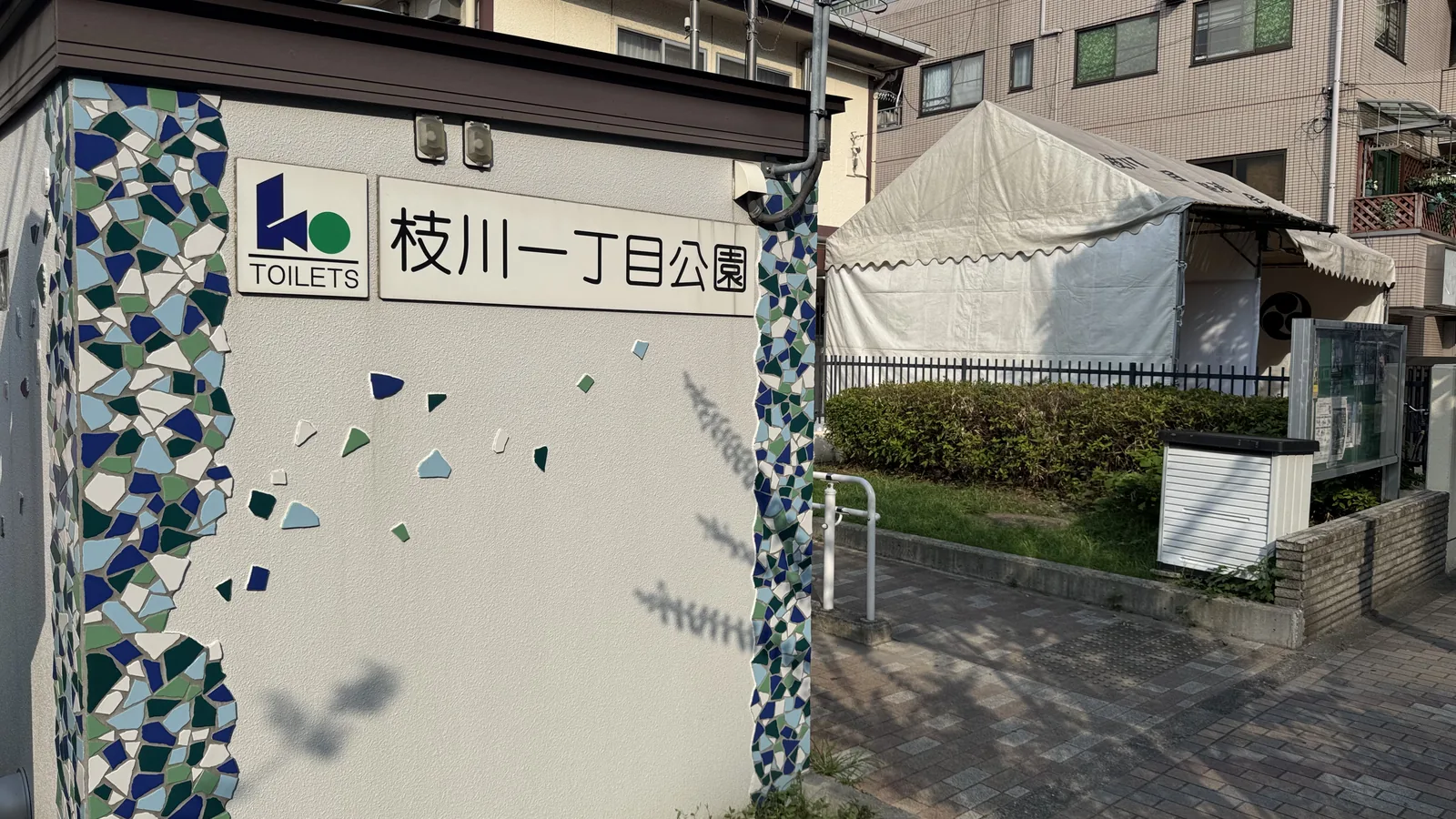 枝川一丁目公園の入口名板と青いモザイク壁。背後にテントと集合住宅