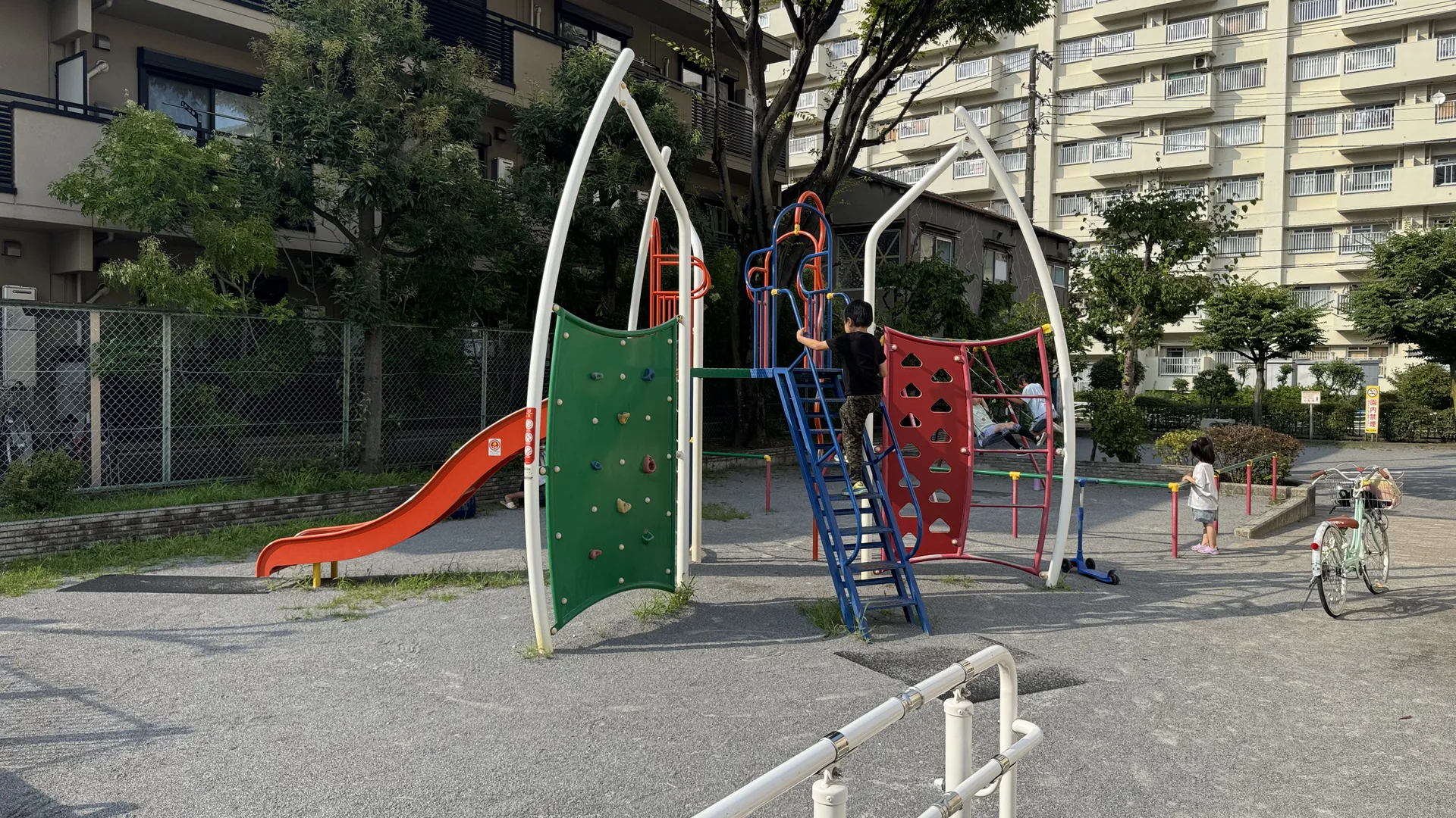 白いアーチの複合遊具が立つ枝川一丁目公園。緑と赤の壁、オレンジのすべり台