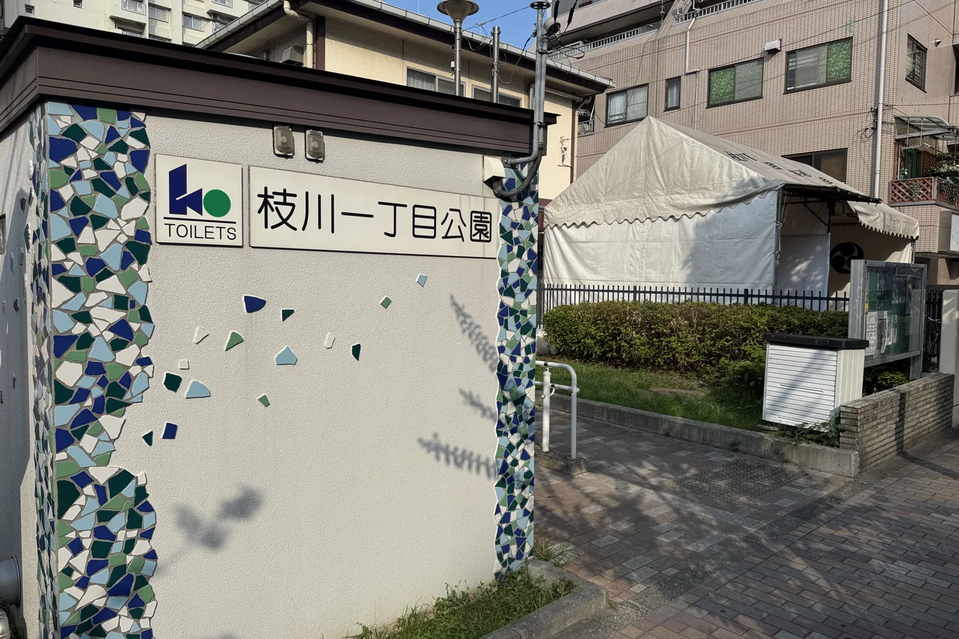 青いモザイクが散る入口壁。枝川一丁目公園の名板とTOILETS表示