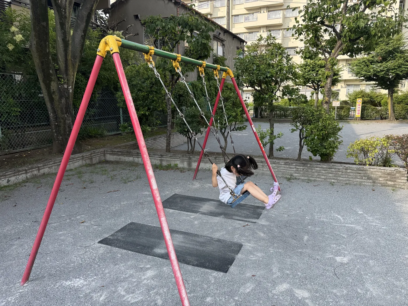 赤緑のフレームのブランコ。足元に黒いゴムマット