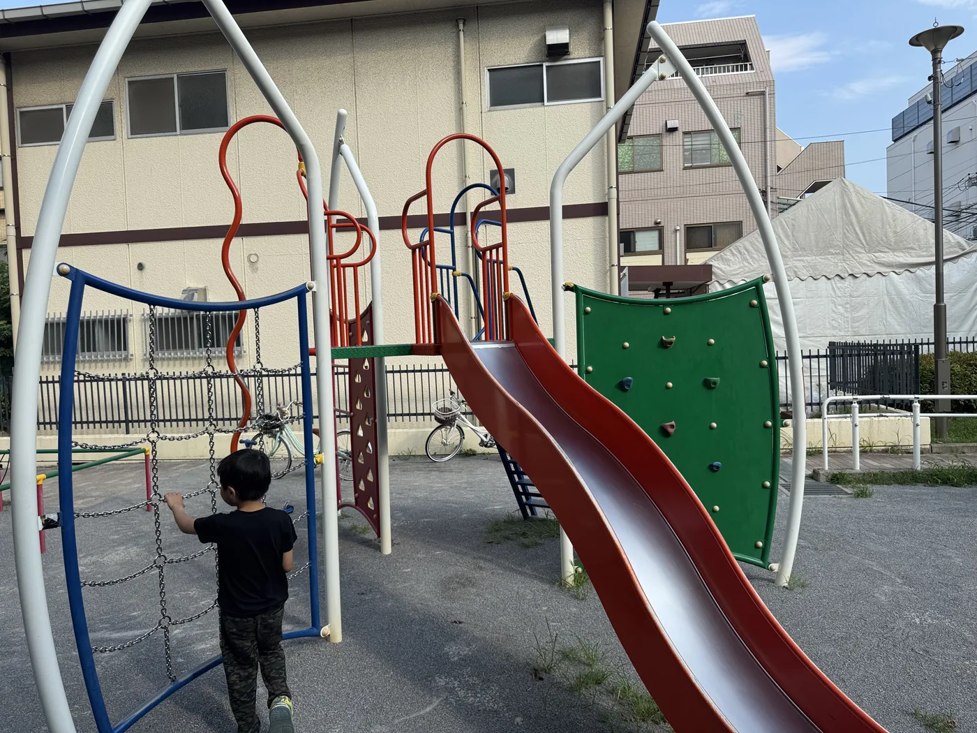 翼形の複合遊具。緑のクライミングウォールと赤いすべり台