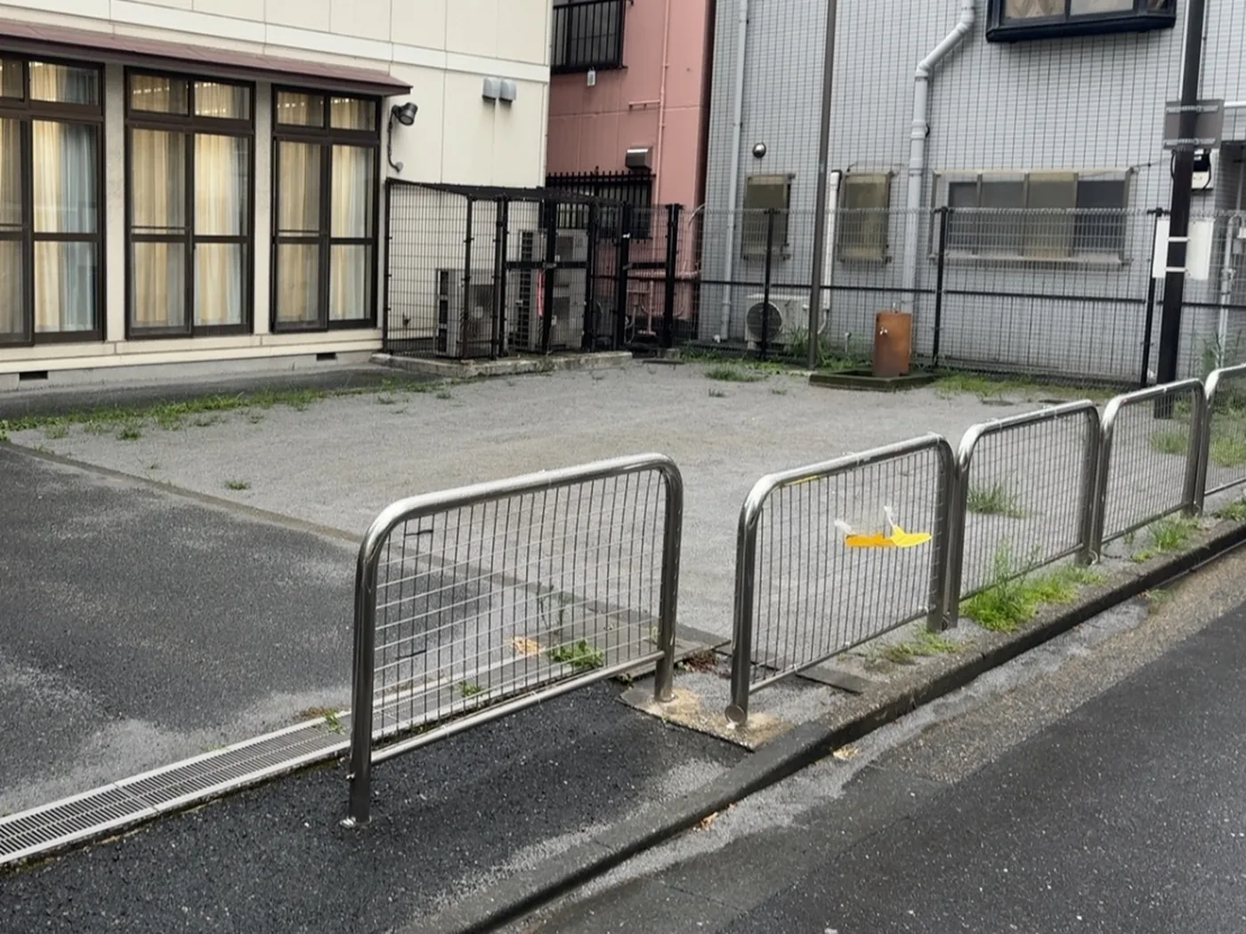 低い金網フェンスの向こうに広がる、雑草のまじった砂利の広場