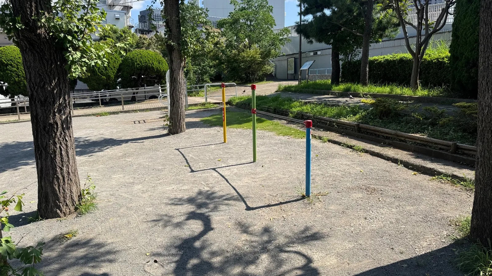 黄・緑・青の支柱の鉄棒と木立