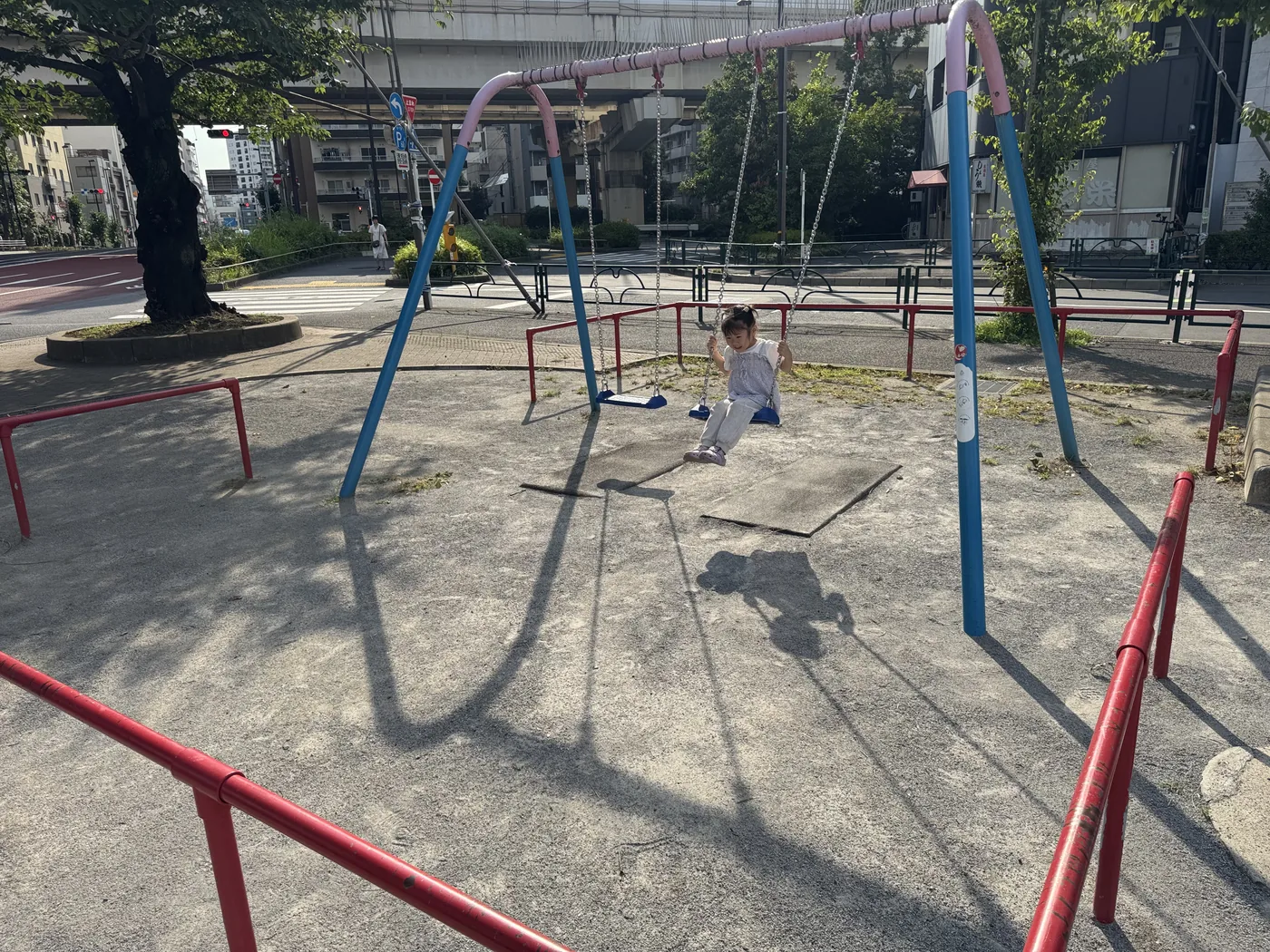ピンクと水色のフレームのブランコと赤い安全囲い