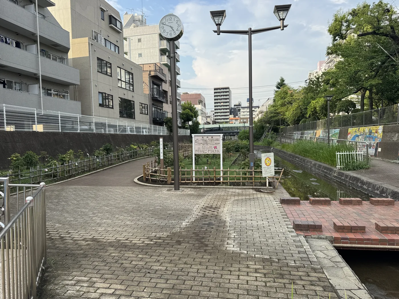 時計と街灯のある広場。水路と花壇、奥に住宅街
