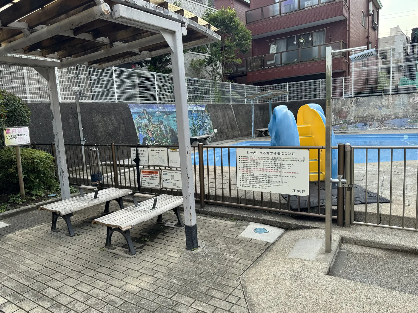 じゃぶじゃぶ池。青い床面の水場と柵、屋根付きベンチ