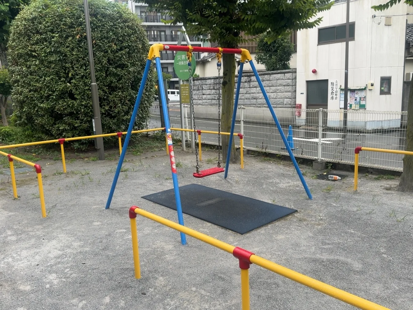 ブランコと遊具まわり。背景に町会防災倉庫の表示