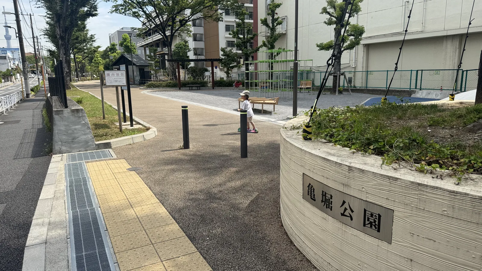 亀堀公園の入口。公園名板と触知ブロック、スカイツリーが遠景に見える