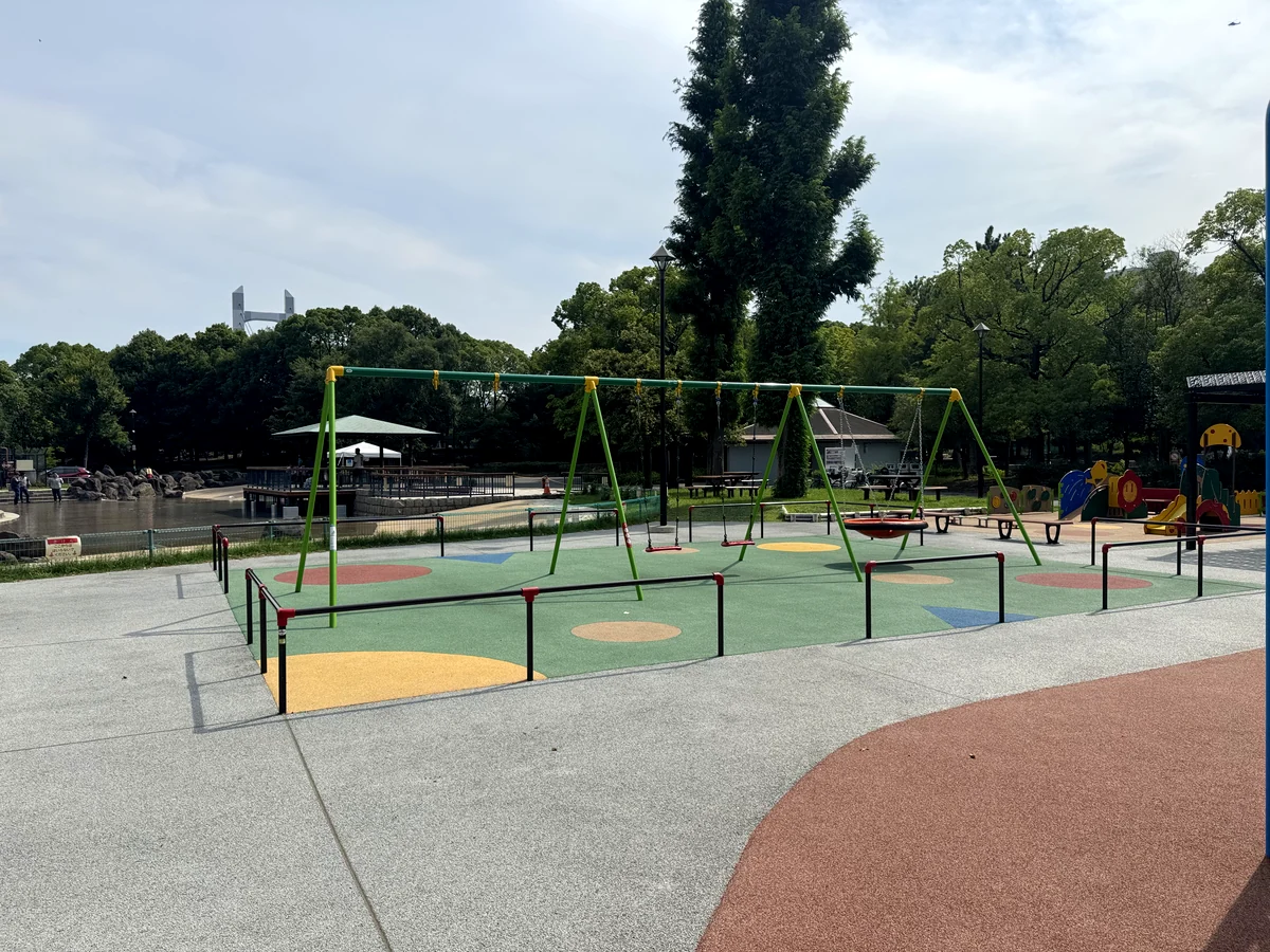 緑のフレームのブランコとネストブランコ。遠くに木場公園大橋