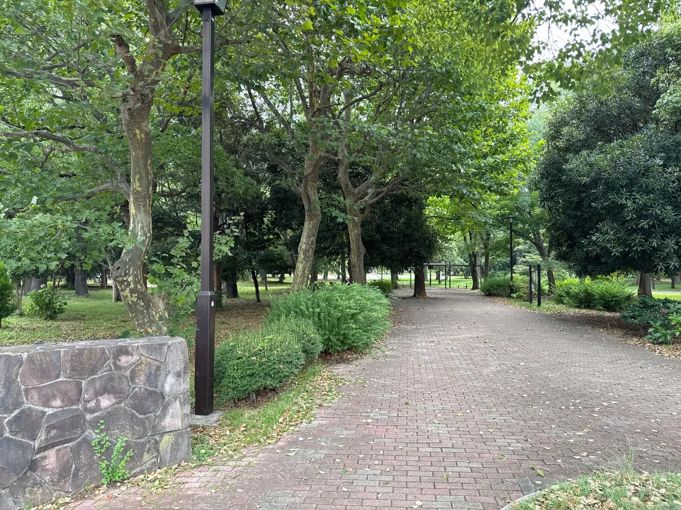 レンガ敷きの園路と石積み、木立の奥へ続く道