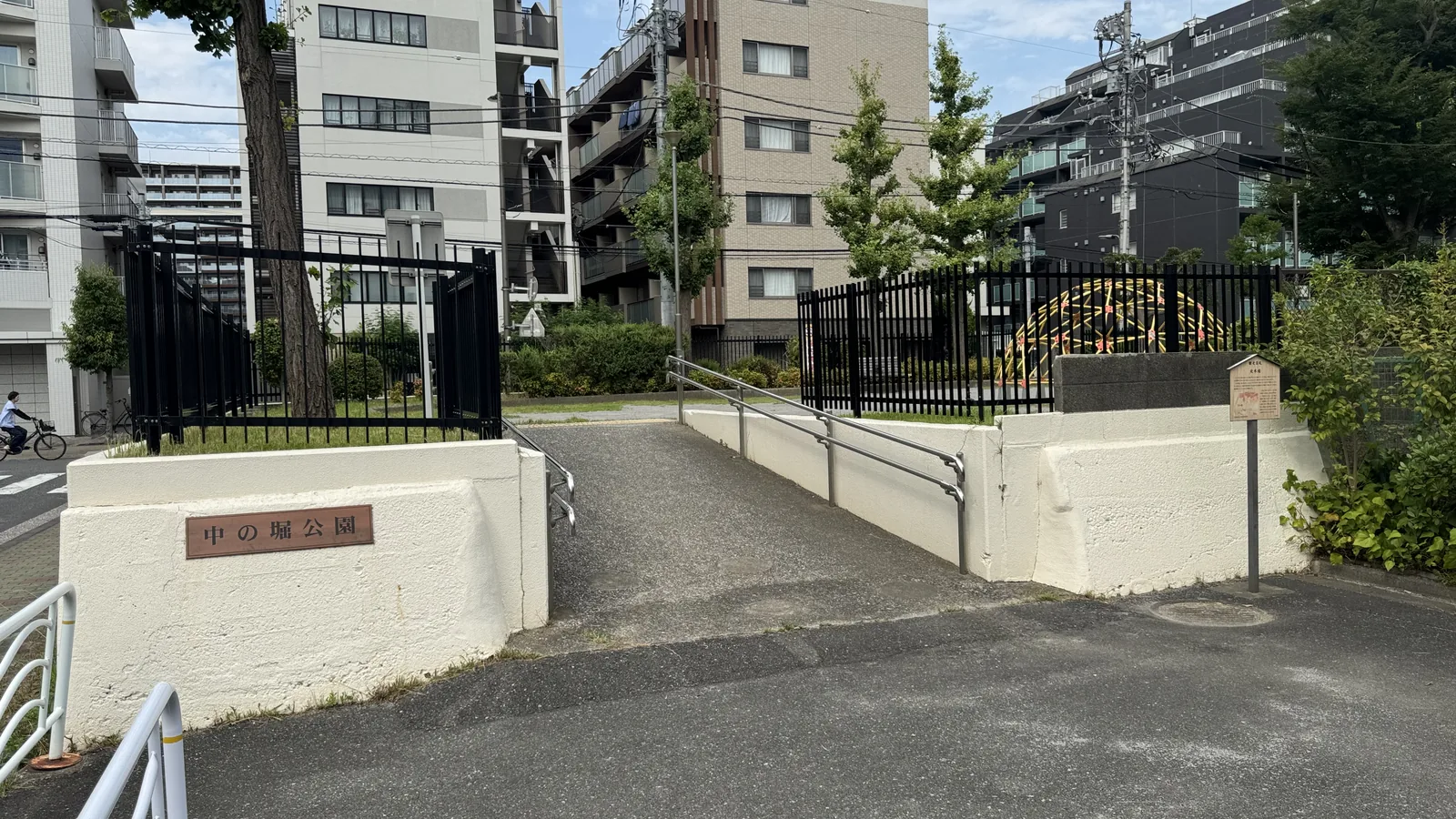 スロープと手すりがある中の堀公園の入口。看板と黒いフェンス