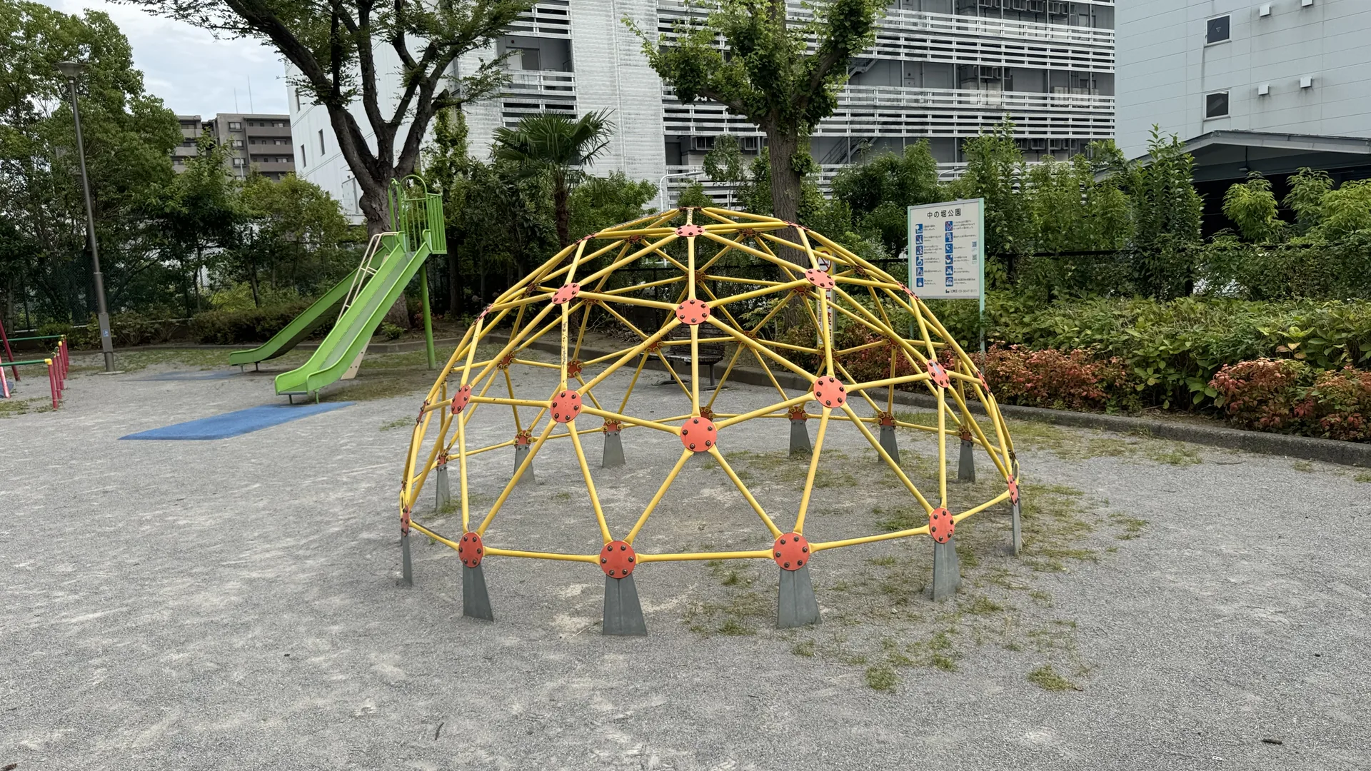 ドーム型ジャングルジムと緑のすべり台が見える中の堀公園の園内