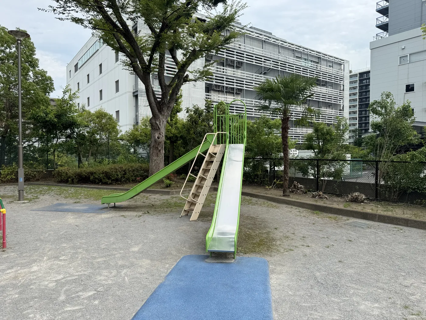 二股の緑すべり台と青い安全マットがある中の堀公園の遊具