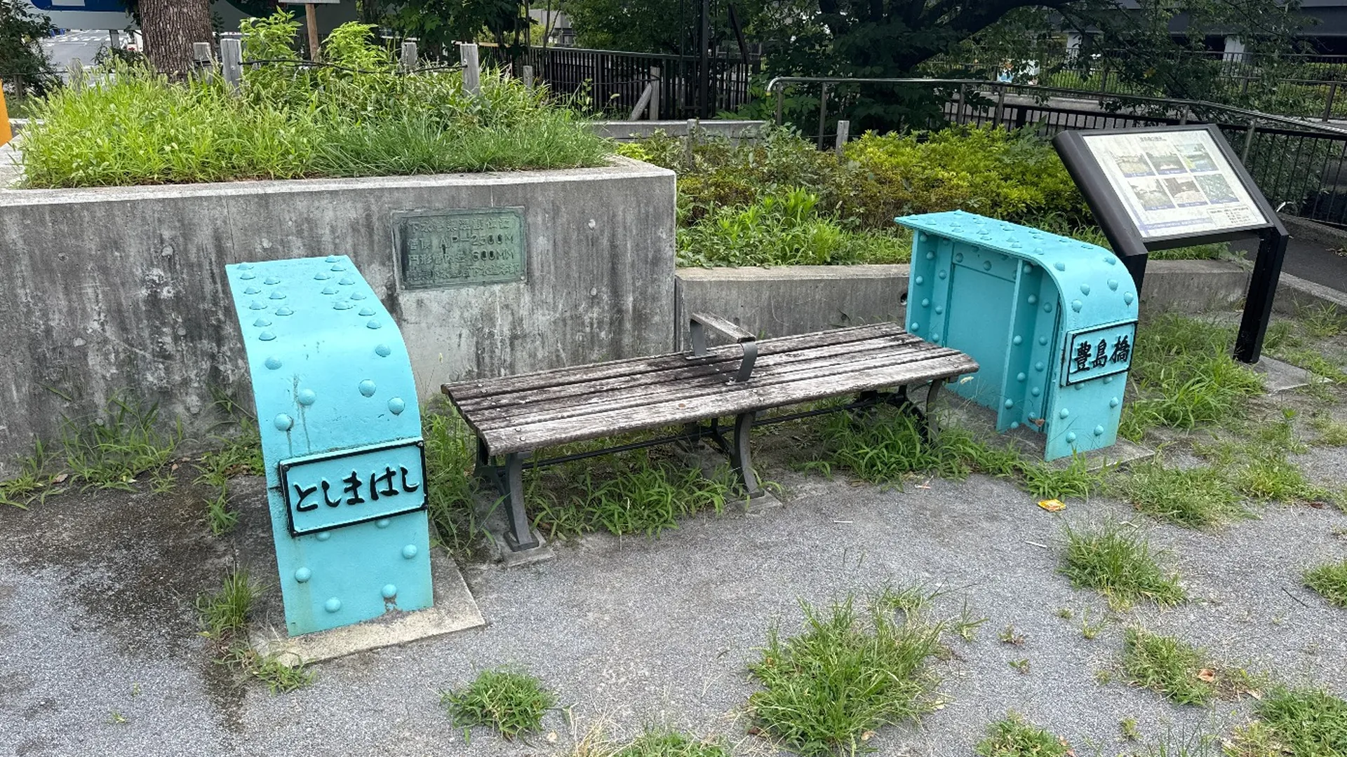 豊島橋の水色鋼材モニュメントに挟まれた木製ベンチと説明板