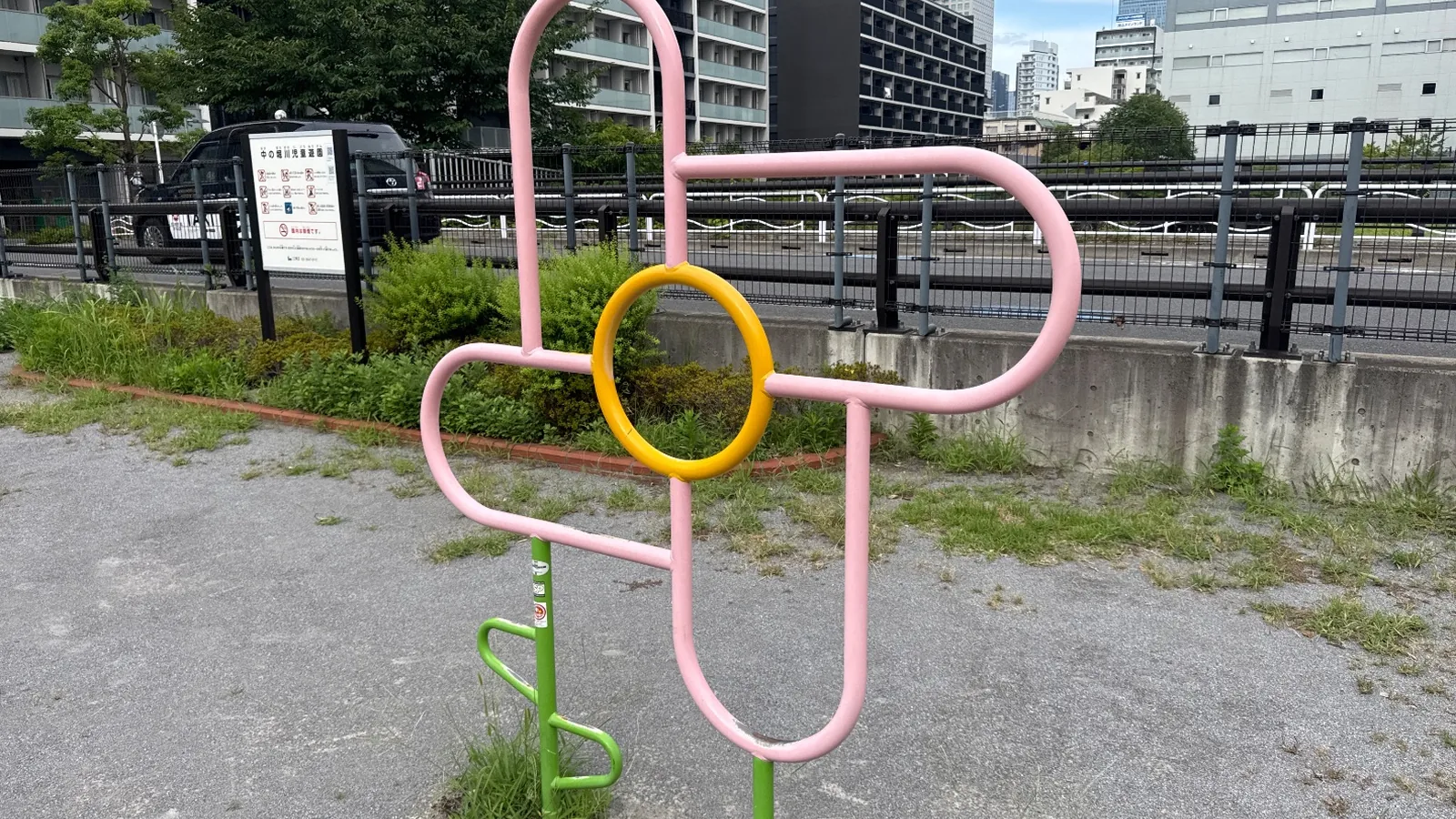 ピンクと黄の花形遊具と利用案内板、奥に建物