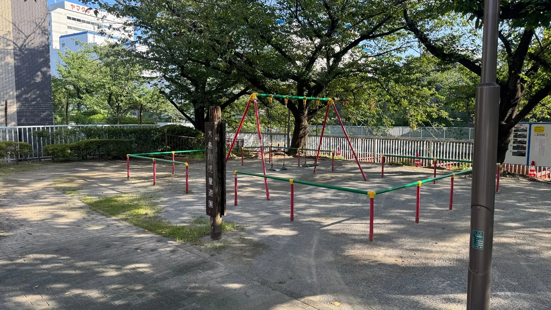 木陰のブランコと園名の木柱。大島川児童遊園の園内