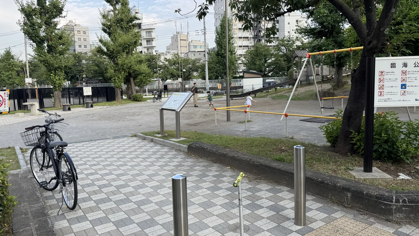チェッカー模様の入口舗装と公園名標識、触知ブロックがある臨海公園の入口