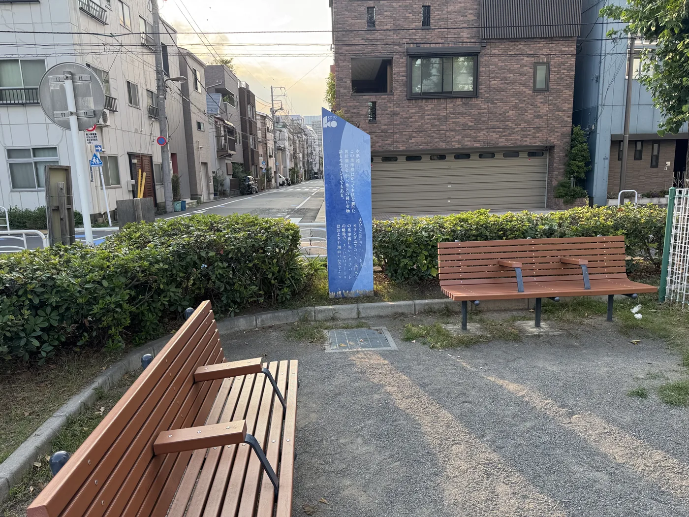 生垣に囲まれた2脚のベンチと青い案内板
