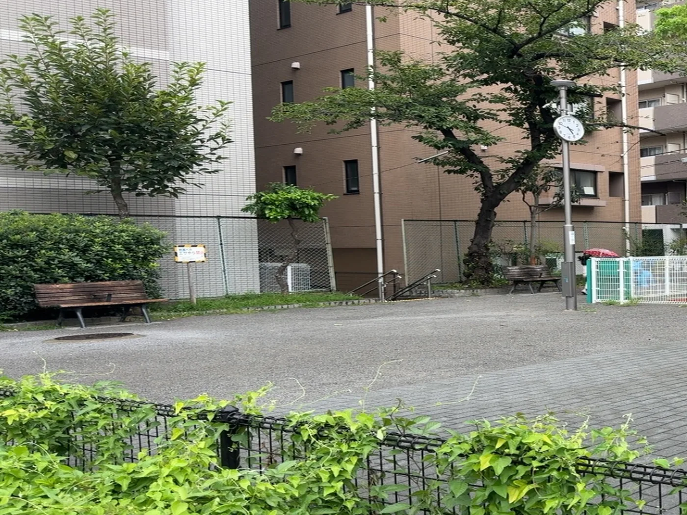 銀のポールの上の時計と、木陰の木製ベンチ