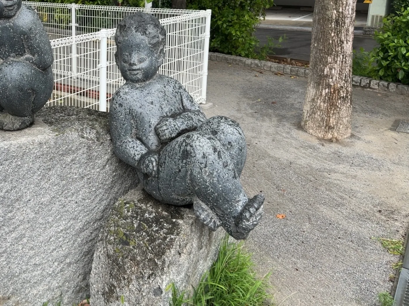 灰色の岩の上に腰かけた、暗い石の子ども像