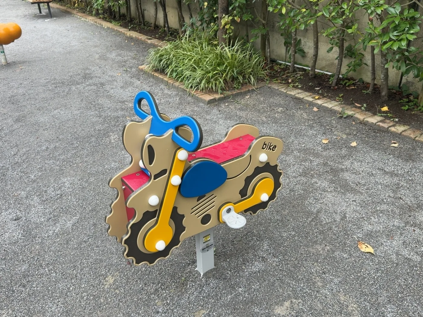 ベージュと青赤黄のバイク型スプリング遊具。後ろにオレンジ色のイモムシ型が見える