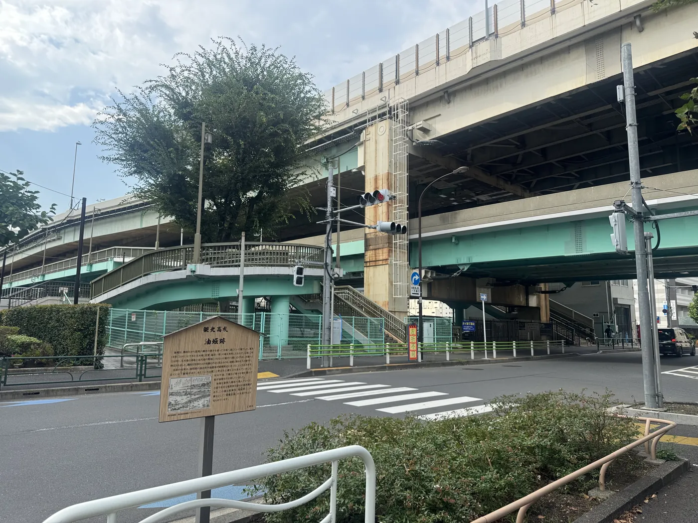 油堀跡の観光高札と、その向こうに重なる首都高速道路のある交差点。