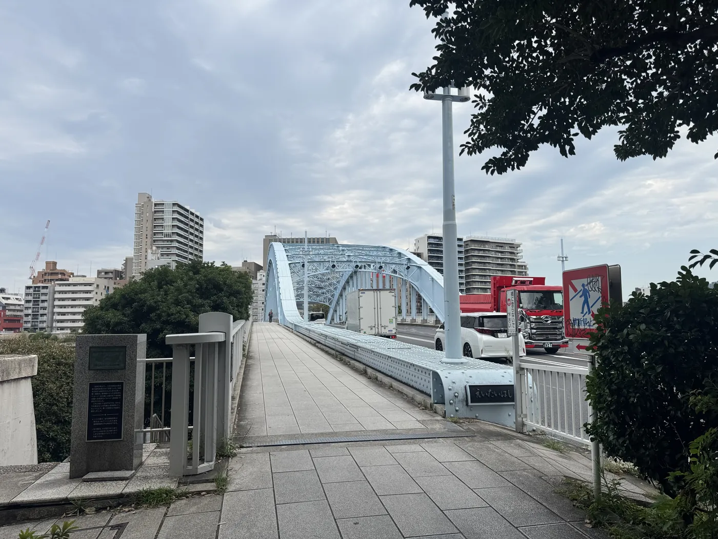 永代橋の歩行者入口から望む水色のアーチ橋と周囲の建物。